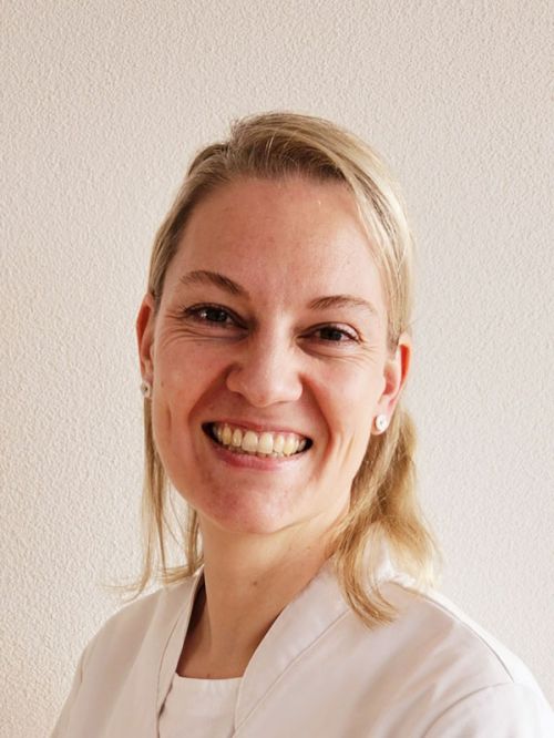 Porträt einer lächelnden Person in weißer Berufskleidung vor neutralem Hintergrund.