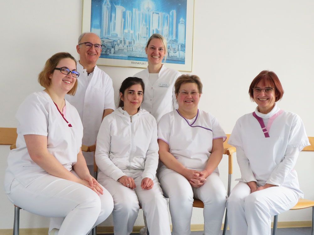 Team der Hausarztpraxis in weißer Berufskleidung posiert gemeinsam für ein Gruppenfoto.
